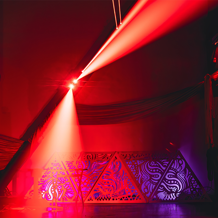 Image imprécise aux tonts rouges présentant deux faisceaux de lumière diffusé par l'équipement d'éclairage, on entrevoit des  silhouettes de décoration en triangle