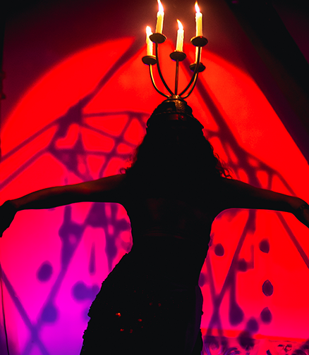 Silhouette de femme sur fond rouge lumineux, portant en équilibre sur la tête un chandelier à 4 bougies, les bras en croix