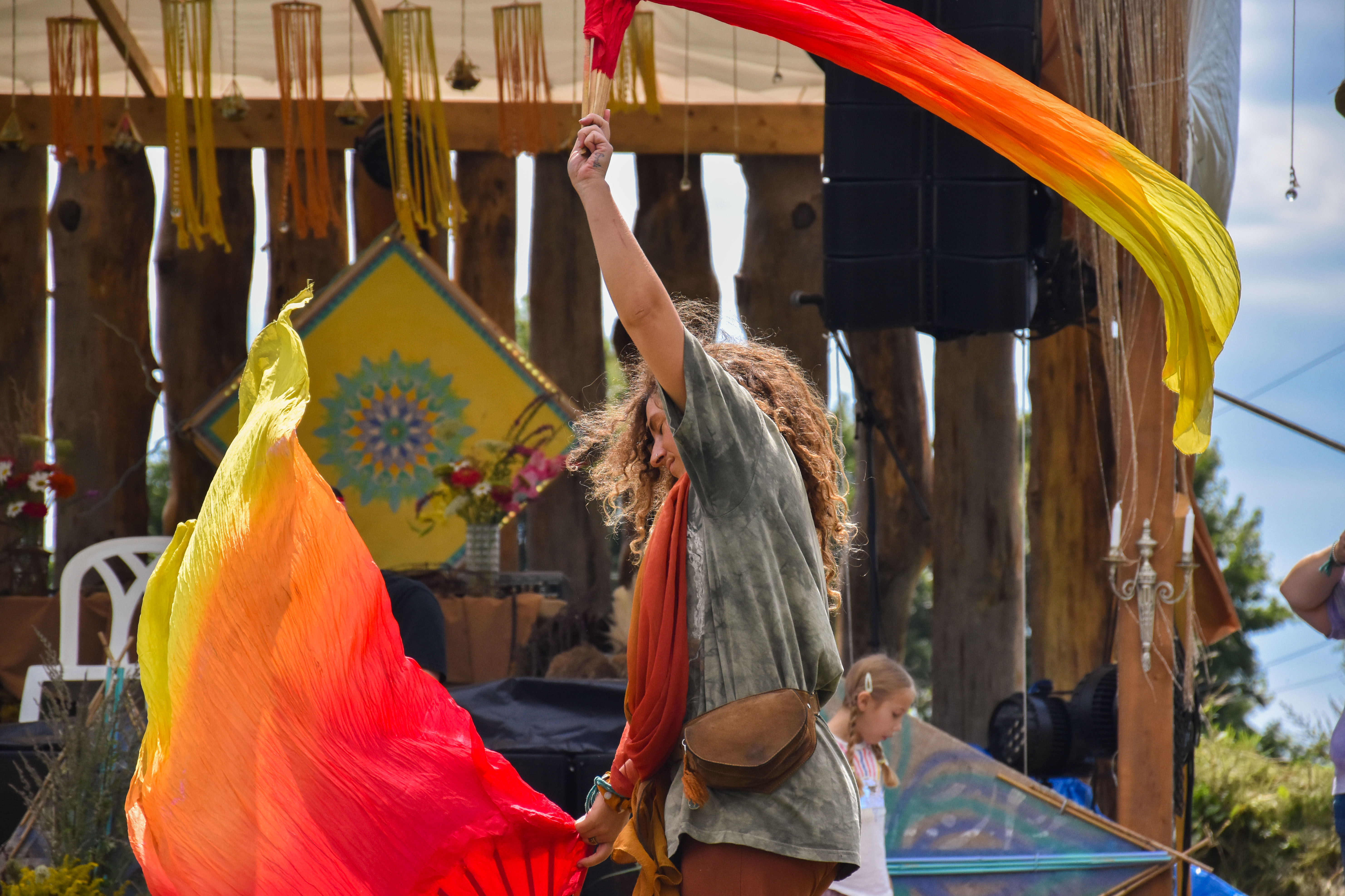 Une fille qui danse avec des évantails de tissus au son d'une musique entraînante diffusé par l'équipement de sonorisation événementiel devant une scène extérieure